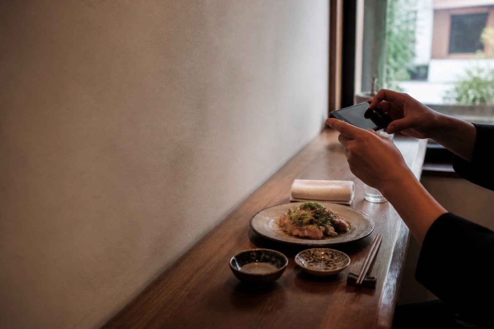 カウンターの料理にスマートフォンを向けて撮影しようとしている手元。